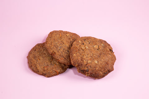 Carrot cake cookies with visible carrot shreds baked to a golden brown color and arranged on a light pink background.