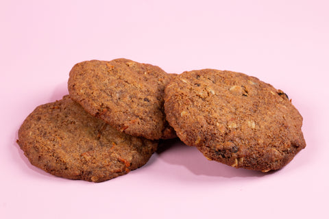 Carrot cake cookies with visible carrot shreds baked to a golden brown color and arranged on a light pink background.
