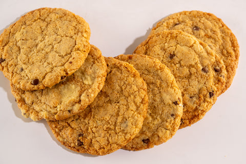 A set of six golden-brown chocolate chip cookies, displayed on a white background. The cookies are slightly chewy with visible chocolate chips.