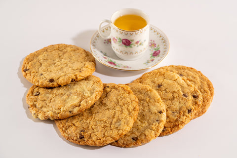 A set of six golden-brown chocolate chip cookies, displayed on a white background with a delicious cup of tea in a beautifully ornate teacup. The cookies are slightly chewy with visible chocolate chips.