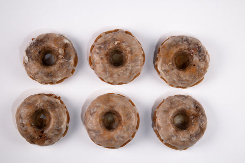 Mini bundt-style cinnamon donuts with vanilla glaze and cinnamon dust arranged in rows on a white background, showcasing their golden-brown color and dripping glaze.