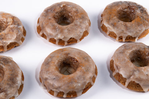 Mini bundt-style cinnamon donuts with vanilla glaze and cinnamon dust arranged in rows on a white background, showcasing their golden-brown color and dripping glaze.