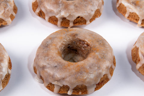 Mini bundt-style cinnamon donuts with vanilla glaze and cinnamon dust arranged in rows on a white background, showcasing their golden-brown color and dripping glaze.