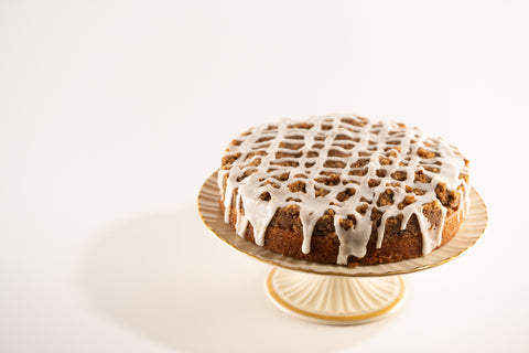 A side view of a round cinnamon crumb cake topped with a lattice-like white icing drizzle.