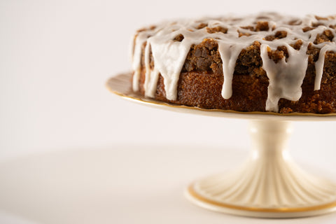 A close-up view of a round cinnamon crumb cake topped with a lattice-like white icing drizzle.