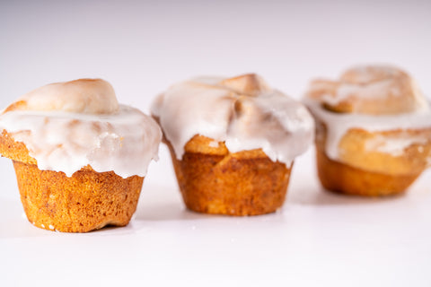 Three cinnamon rolls with a golden-brown exterior, covered in a smooth white glaze. They are arranged in a row on a white surface.