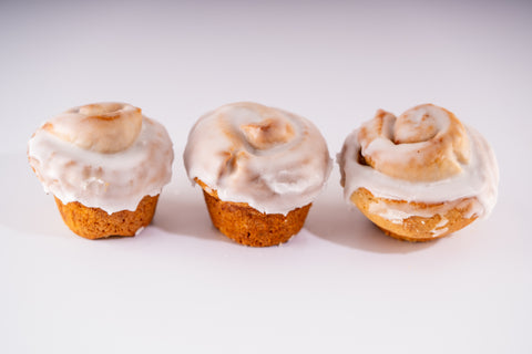 Three cinnamon rolls with a golden-brown exterior, covered in a smooth white glaze. They are arranged in a row on a white surface.