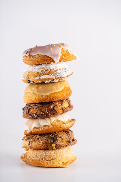 A tall stack of donuts, each featuring various toppings. The donuts are arranged vertically, showcasing a variety of textures, including powdered sugar, chocolate drizzle, and icing.