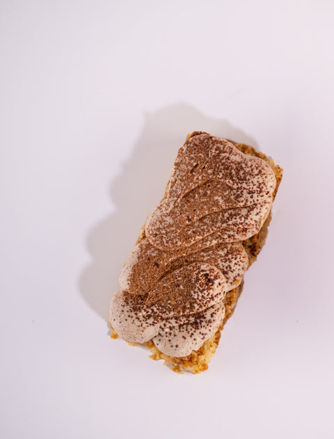 A rectangular tiramisu dessert dusted with cocoa powder on a white background.