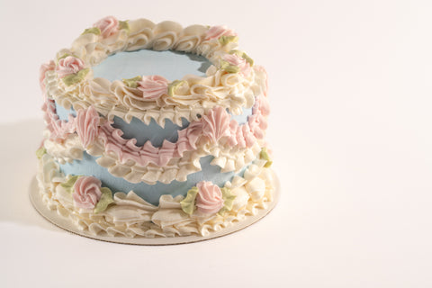 A side view of a vegan and gluten-free vintage cake with detailed floral buttercream piping in white, pink, and green, set against a pastel blue frosting base.