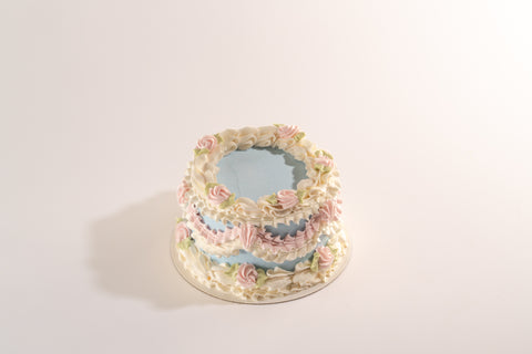 A top-down view of a vegan and gluten-free vintage cake with pastel blue frosting, decorated with intricate white and pink buttercream swirls and green leaf accents.