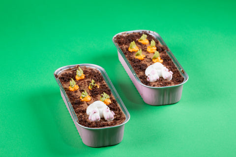 A chocolate mini cake featuring a white bunny bottom with pink paws and orange carrot sprouts against chocolate frosting and crumbs.