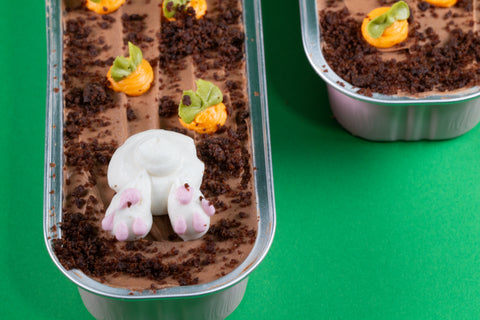 Detailed view of chocolate mini cake featuring a white bunny bottom with pink paws and orange carrot sprouts against chocolate frosting and crumbs.