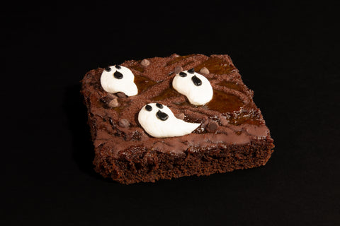 Fudgy chocolate brownie decorated with three white frosting ghost shapes with chocolate chip faces - allergy-friendly Halloween dessert side angle view