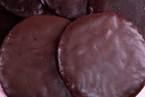 A close-up view of five round, flat chocolate thin mint cookies stacked on top of each other on a pink surface.