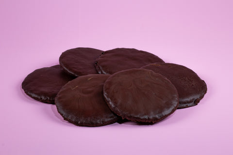 A top view of six round, flat chocolate thin mint cookies stacked on top of each other on a pink surface.