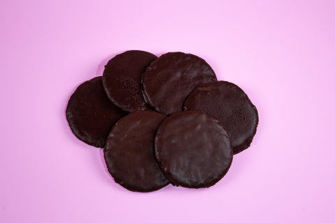 A top view of six round, flat chocolate thin mint cookies stacked on top of each other on a pink surface.