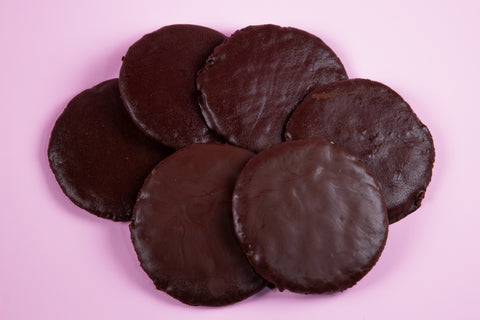 A top view of six round, flat chocolate thin mint cookies stacked on top of each other on a pink surface.