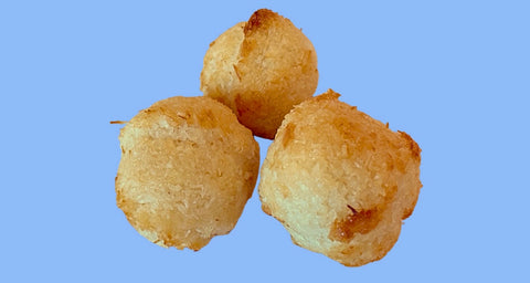 Three golden-brown coconut macaroons against a blue background. These round, textured treats show a perfect golden exterior with visible coconut flakes, demonstrating the gluten-free, kosher, and vegan macaroons available at Erin McKenna's Bakery.