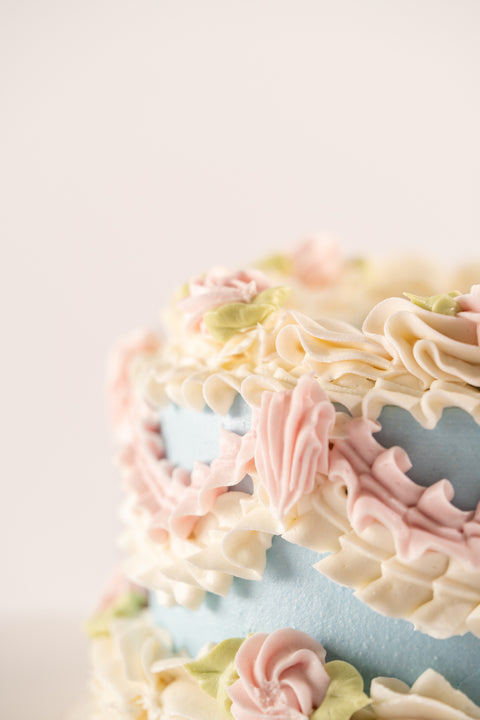 A close-up view of a vegan and gluten-free vintage cake, highlighting the delicate buttercream floral designs in pastel colors.