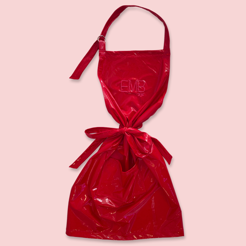 Zoomed out view of a shiny red apron featuring the embroidered initials 'EMB NYC' on the front.