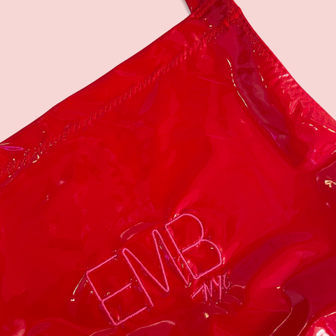 Close-up view of a shiny red apron featuring the embroidered initials 'EMB NYC' on the front.