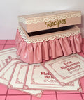 Blush recipe box with lace details on a pink tile floor 
