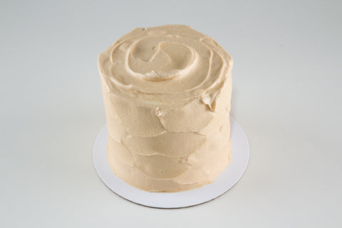 Beige frosted cake on a white stand against a light gray background