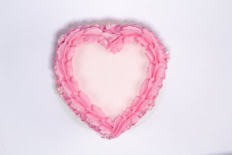 Romantic heart-shaped cake with layered pink buttercream ruffles and vintage-style Valentine's piping on a white cake board