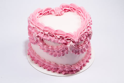 Romantic heart-shaped cake with layered pink buttercream ruffles and vintage-style Valentine's piping on a white cake board