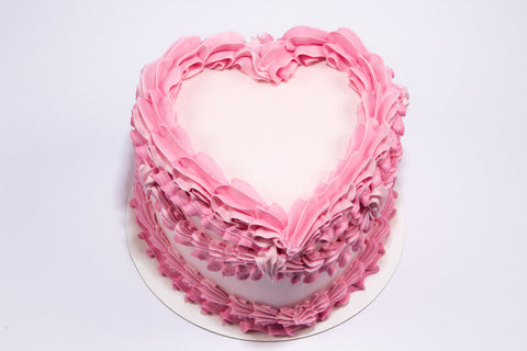 Romantic heart-shaped cake with layered pink buttercream ruffles and vintage-style Valentine's piping on a white cake board