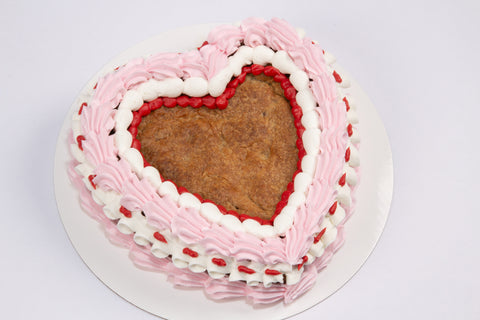 Heart-shaped chocolate chip cookie cake decorated with pink and white vegan buttercream rosettes and red piping details on a white cake board