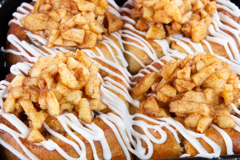 Close-up of four apple cinnamon rolls topped with diced apple pieces and white drizzle icing in a baking pan.