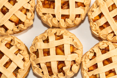 Overhead close-up shot of six artisanal apple pie cupcakes showcasing detailed vanilla frosting lattice work and ruffled edges, with golden apple filling peeking through the design