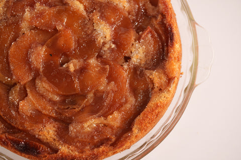 A close-up of a vegan, gluten-free apple upside-down cake with caramelized apple slices arranged in a circular pattern on top, with a golden-brown crust.