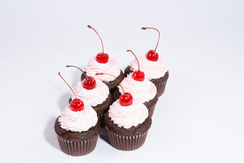 Chocolate cupcakes topped with swirled pink dairy-free buttercream frosting and glossy maraschino cherries on white background