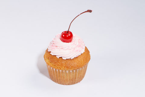 Vanilla cupcake topped with swirled pink dairy-free buttercream frosting and glossy maraschino cherries on white background