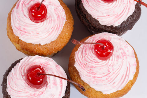 Vanilla and chocolate cupcakes topped with swirled pink dairy-free buttercream frosting and glossy maraschino cherries on white background