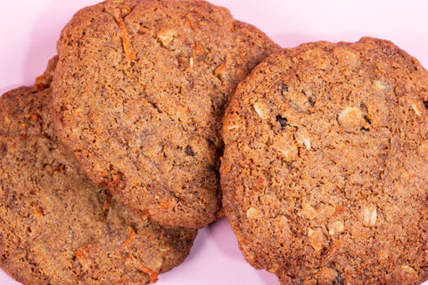Carrot cake cookies with visible carrot shreds baked to a golden brown color and arranged on a light pink background.