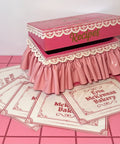 Hot pink recipe box with lace details on a pink tile floor 