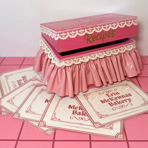 Hot pink recipe box with lace details on a pink tile floor 