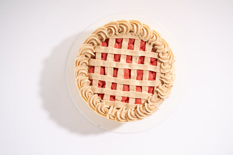 A vegan cherry pie cake with intricate lattice-like frosting and bright cherry filling.