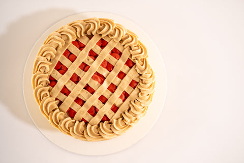 A vegan cherry pie cake with intricate lattice-like frosting and bright cherry filling.