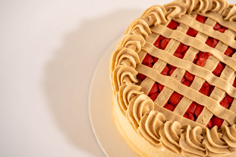 A side angle of a cherry pie-inspired cake, showcasing the piped frosting around the edges and vibrant cherry filling.