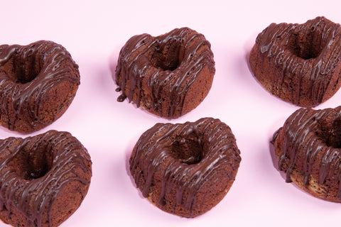 Heart-shaped mini chocolate donuts with chocolate drizzle arranged on pink background

