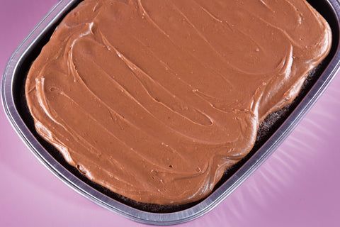 Chocolate frosted cake in a pan on a pink background