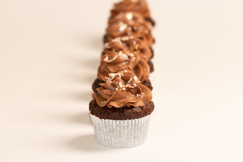 Row of chocolate brownie cupcakes topped with swirled chocolate peppermint frosting and crushed candy cane pieces on cream background