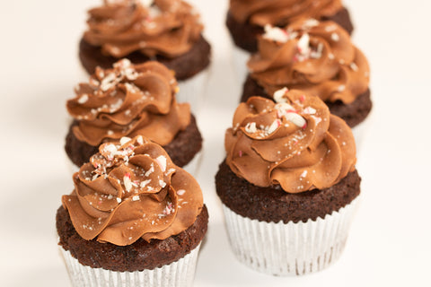 Group of chocolate brownie cupcakes showcasing perfectly piped peppermint chocolate frosting topped with holiday candy cane pieces