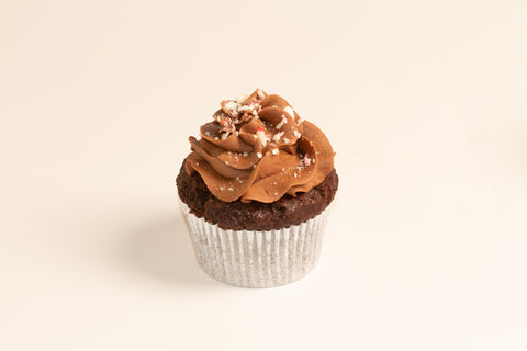 Single peppermint chocolate brownie cupcake displaying rich chocolate frosting swirls and sprinkled candy cane pieces against neutral background