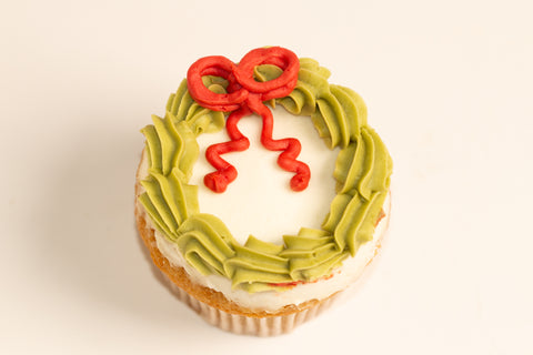 Vanilla cupcake decorated as a Christmas wreath with piped green frosting border and red bow with trailing ribbons